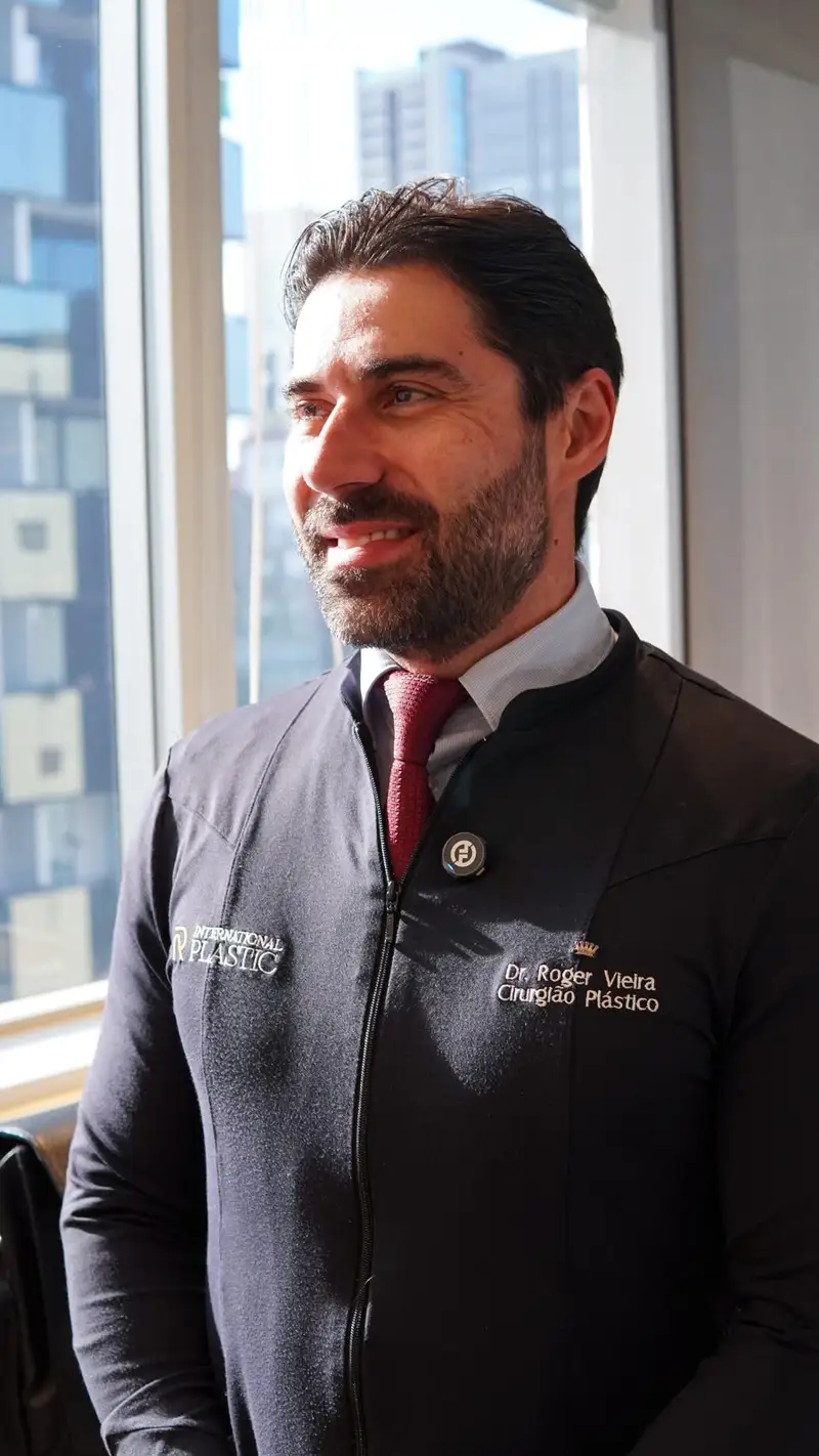 Dr. Roger Vieira sorrindo, de uniforme da clínica